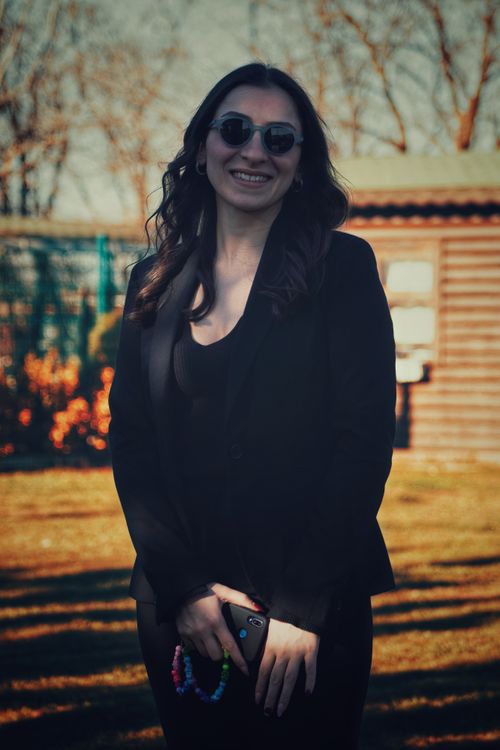 Free Stylish woman wearing sunglasses and black blazer, smiling outdoors in daylight. Stock Photo
