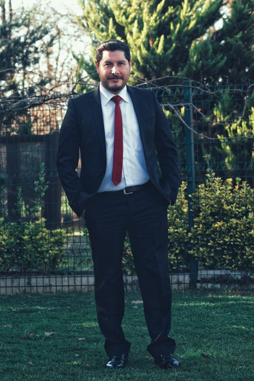 Free Portrait of a man in a suit and red tie posing outdoors in a garden setting. Stock Photo