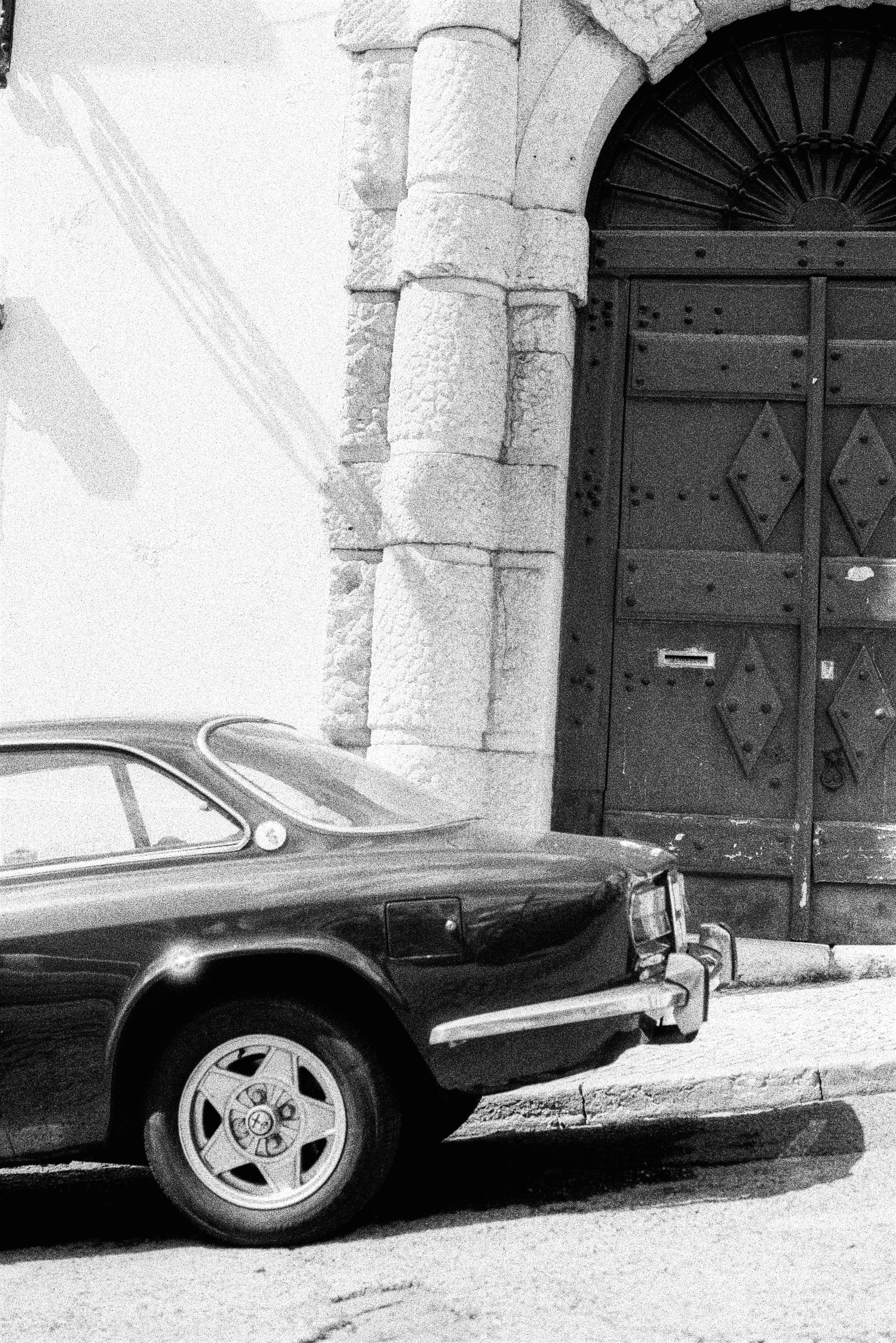 Black and white photo of a classic car parked by a stone archway in Lisbon, Portugal.