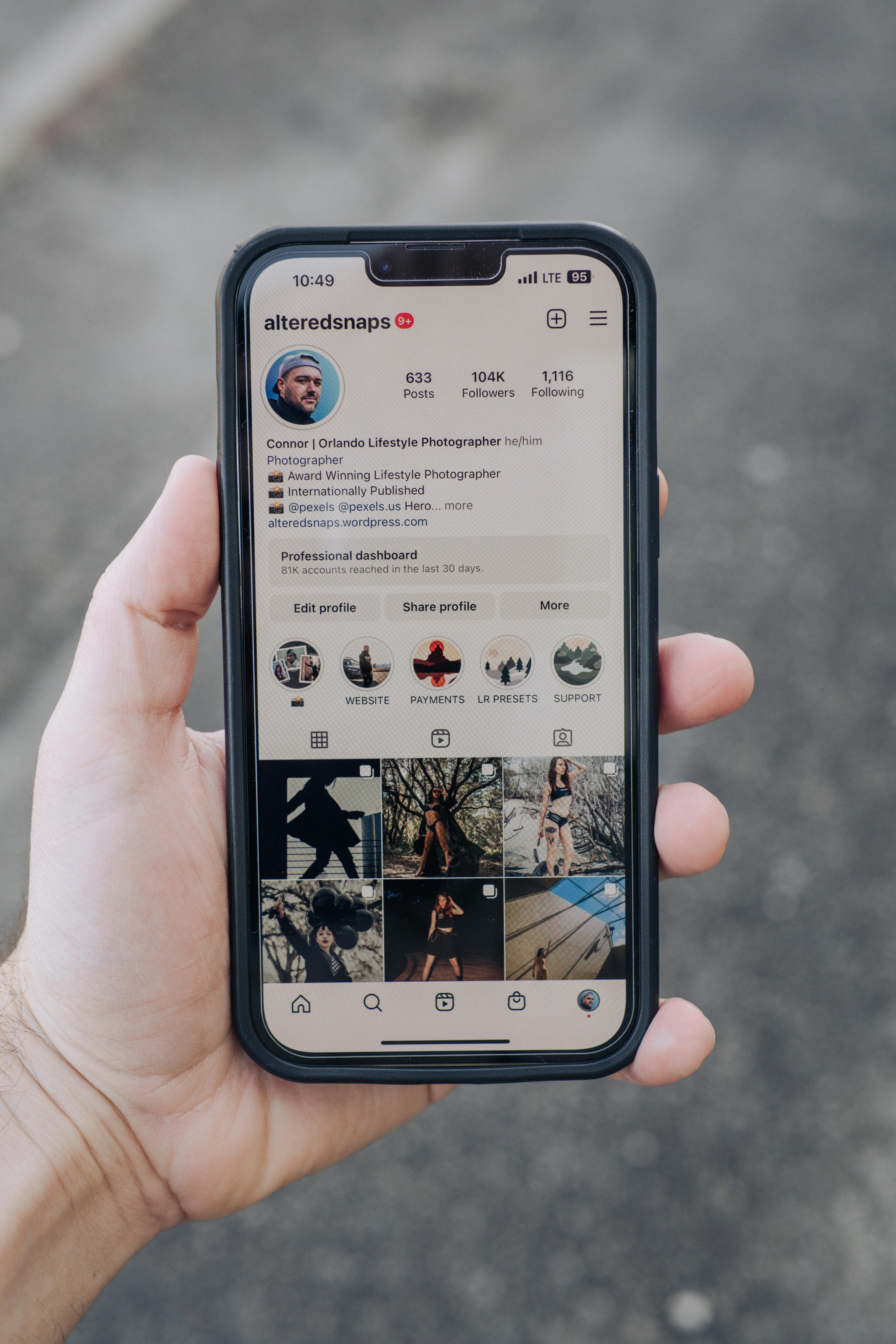 Close-up of a hand holding a smartphone showing a social media profile outdoors.