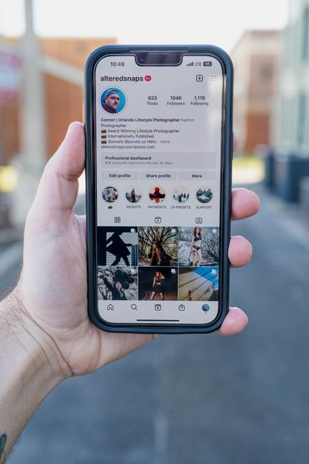 Hand holding a smartphone with an Instagram profile visible, set against a blurred street background.