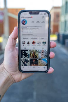 Close-up of a hand holding a smartphone displaying an Instagram profile outdoors.