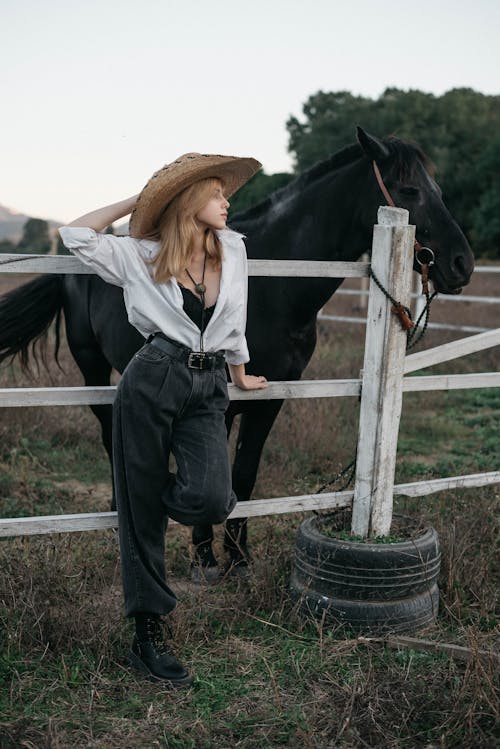 Woman Wearing Cowboy Hat Standing by Fence Next to Horse