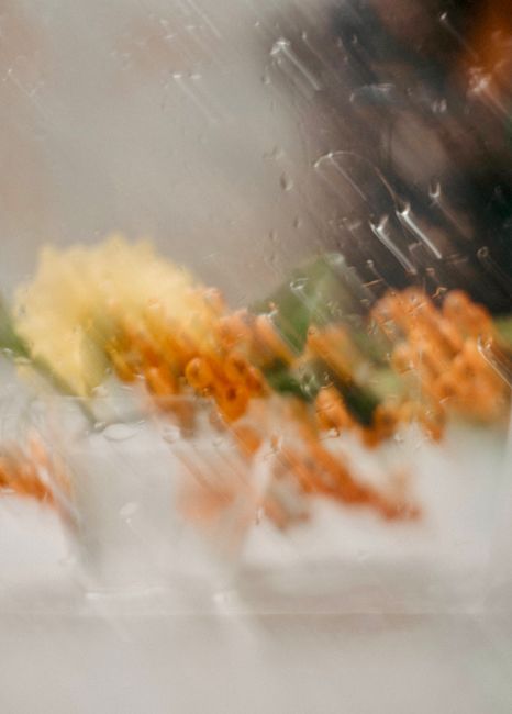 Blurry flowers seen through raindrop-covered glass, creating an abstract and artistic view.