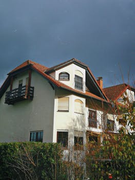 A traditional house with red tiles against a dark sky, surrounded by greenery.