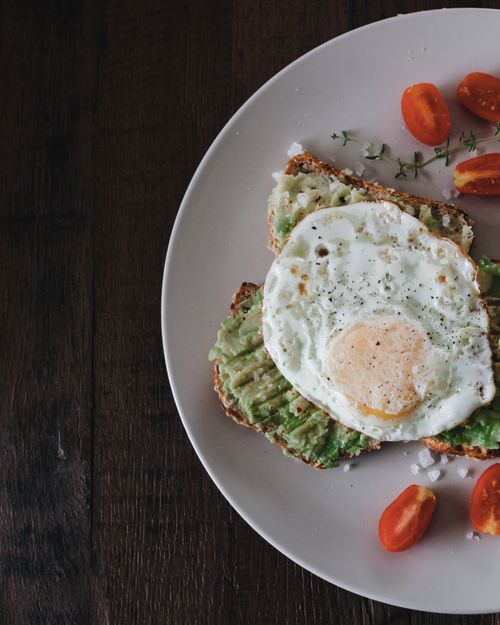 Free Tasty avocado toast topped with a perfectly fried egg, garnished with cherry tomatoes. Stock Photo