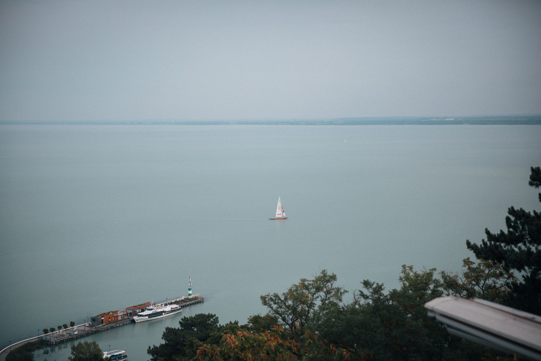A peaceful aerial view of Tihany's coastline with a lone sailboat on a tranquil sea. — photo by Bence Szemerey / Pexels
