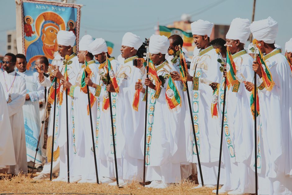 A vibrant Ethiopian religious procession with men in traditional white robes and colorful sashes outdoors.