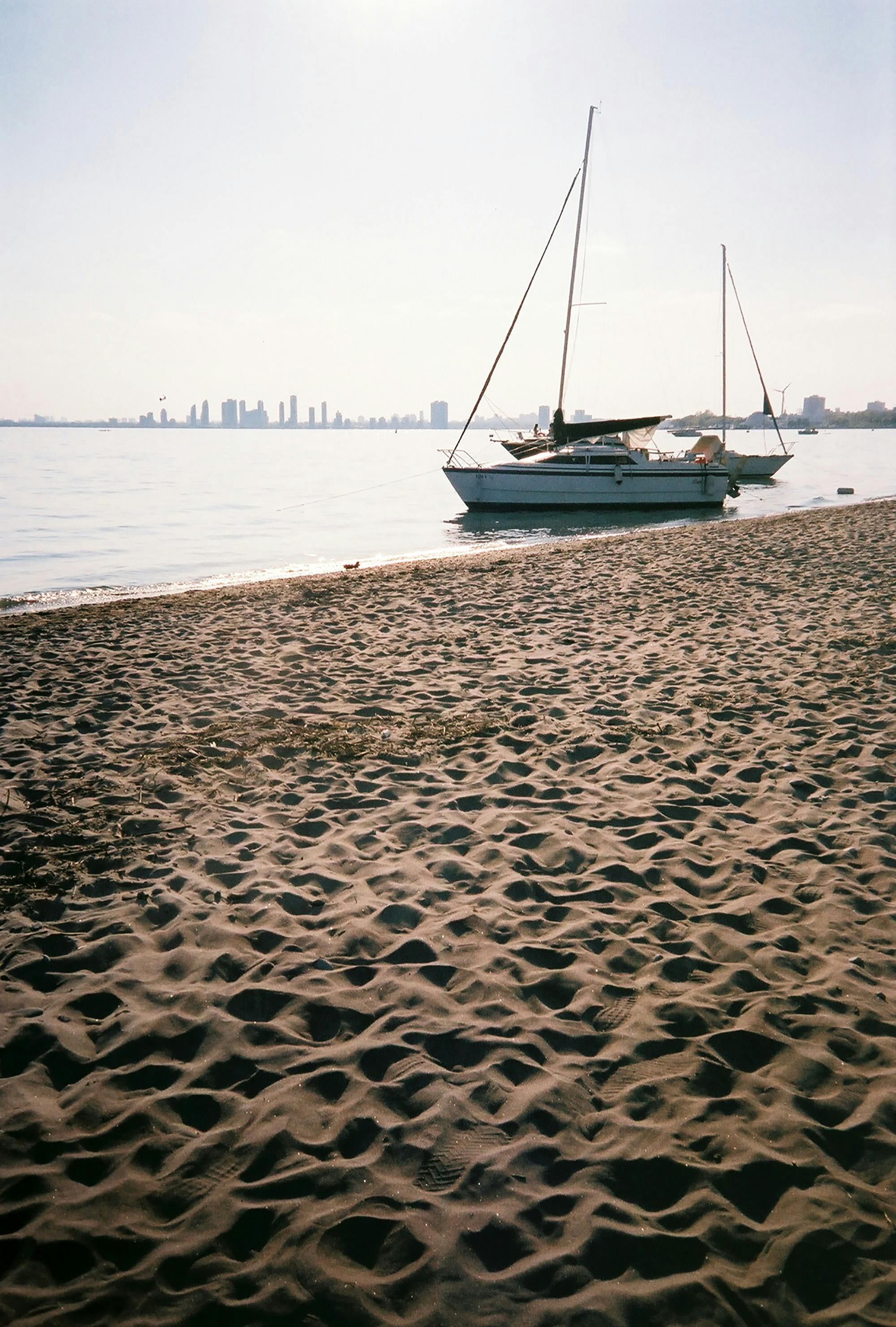 Beautiful sailboats moored on a sandy beach with Toronto skyline in the background.