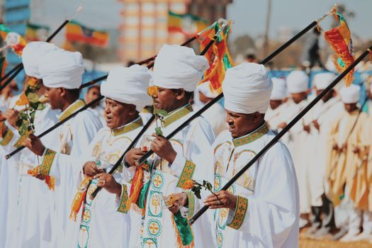 A vibrant Ethiopian cultural parade featuring men in traditional attire holding staffs, celebrating a religious ceremony outdoors.