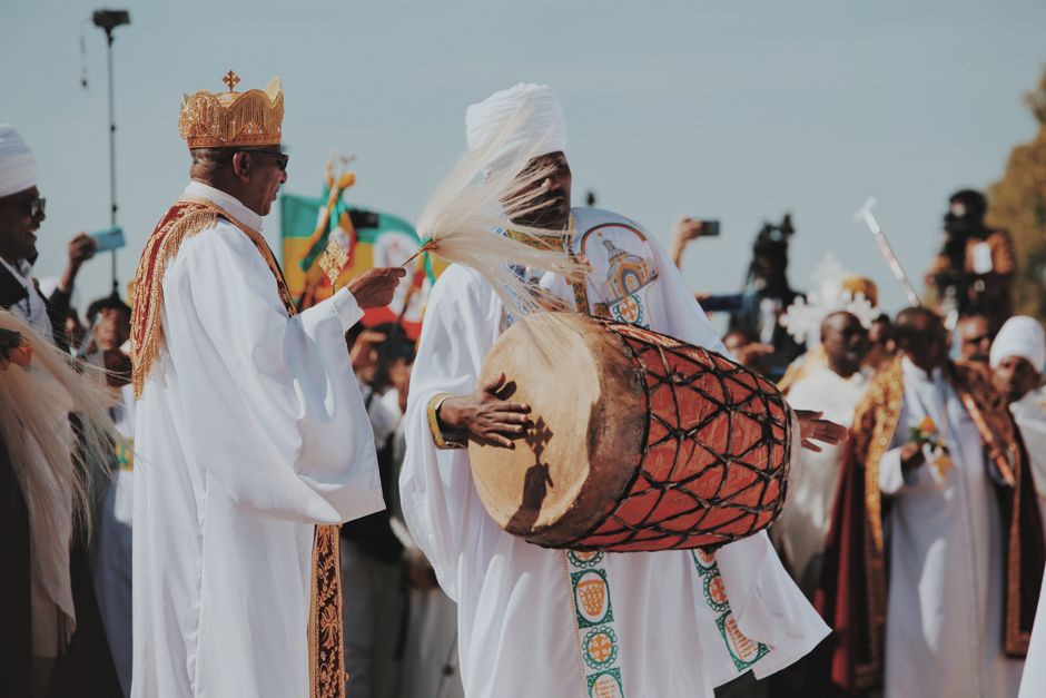 Men in traditional attire playing drums at a vibrant cultural ceremony outdoors.