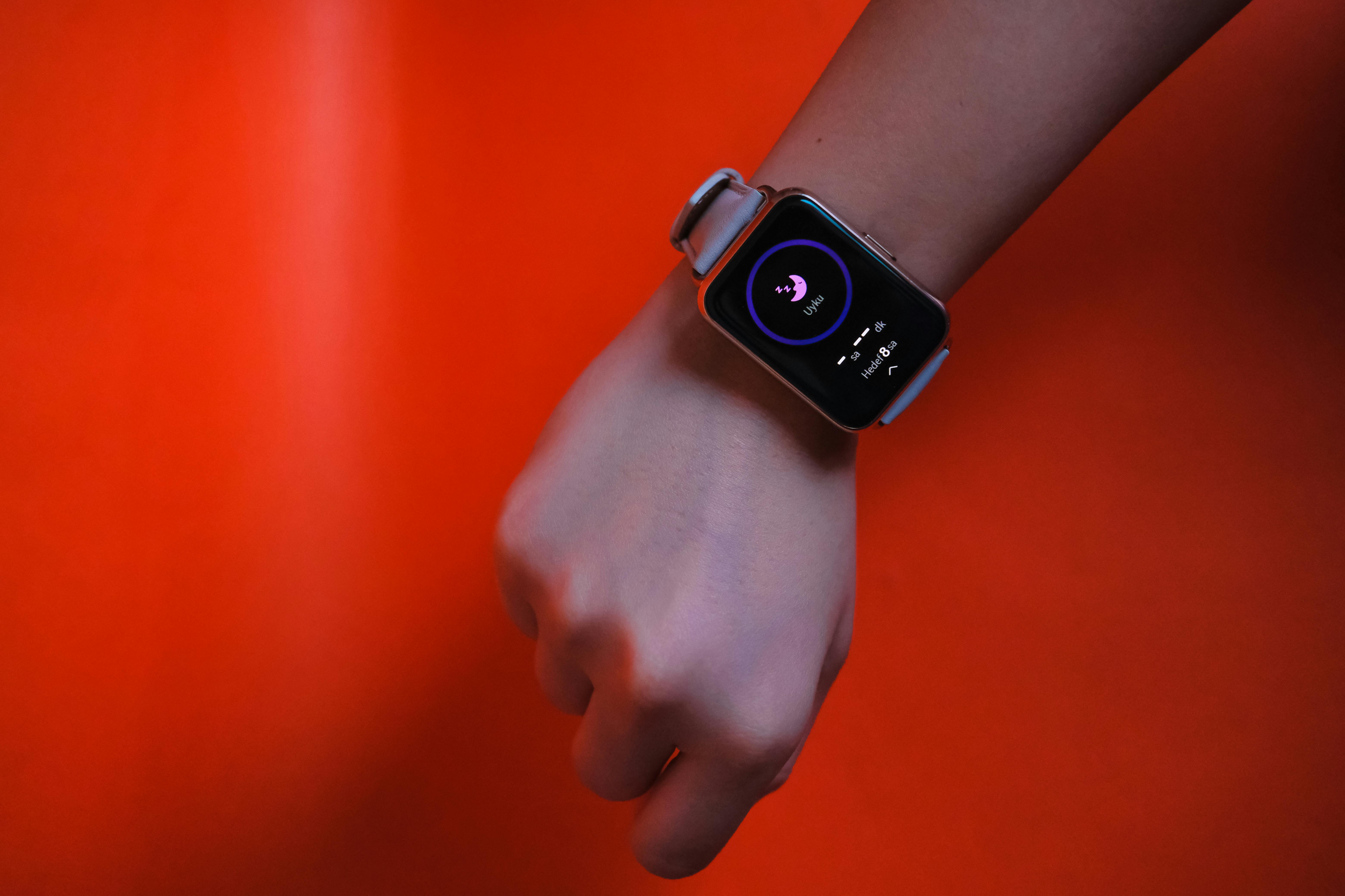 Free Fist wearing a smartwatch with fitness tracking display on a vibrant orange background. Stock Photo