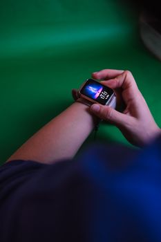 Close-up of hands interacting with a smartwatch in front of a vibrant green background, highlighting modern technology.