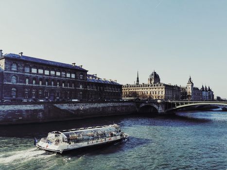 Scenic view of a river cruise boat on the Seine, passing historic buildings and a bridge in Paris, France.