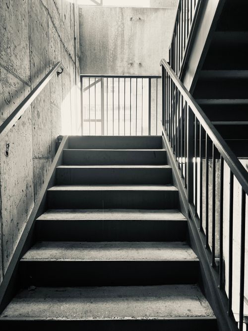 Free Black and white photo of an empty urban indoor staircase illuminated by sunlight. Minimalist and architectural. Stock Photo