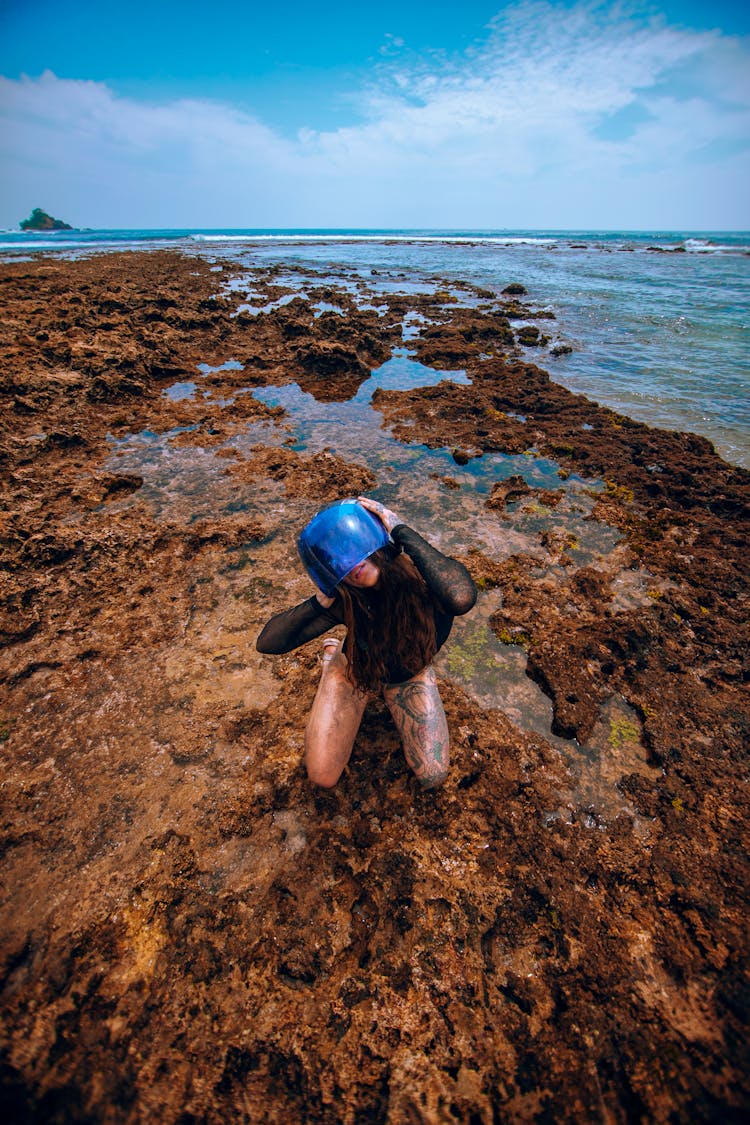 Woman Crouching With Pot On Mud On Beach