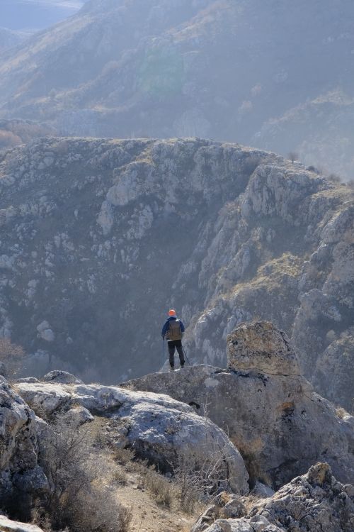 Free A lone hiker stands atop a rocky cliff, overlooking a vast mountain range. Stock Photo