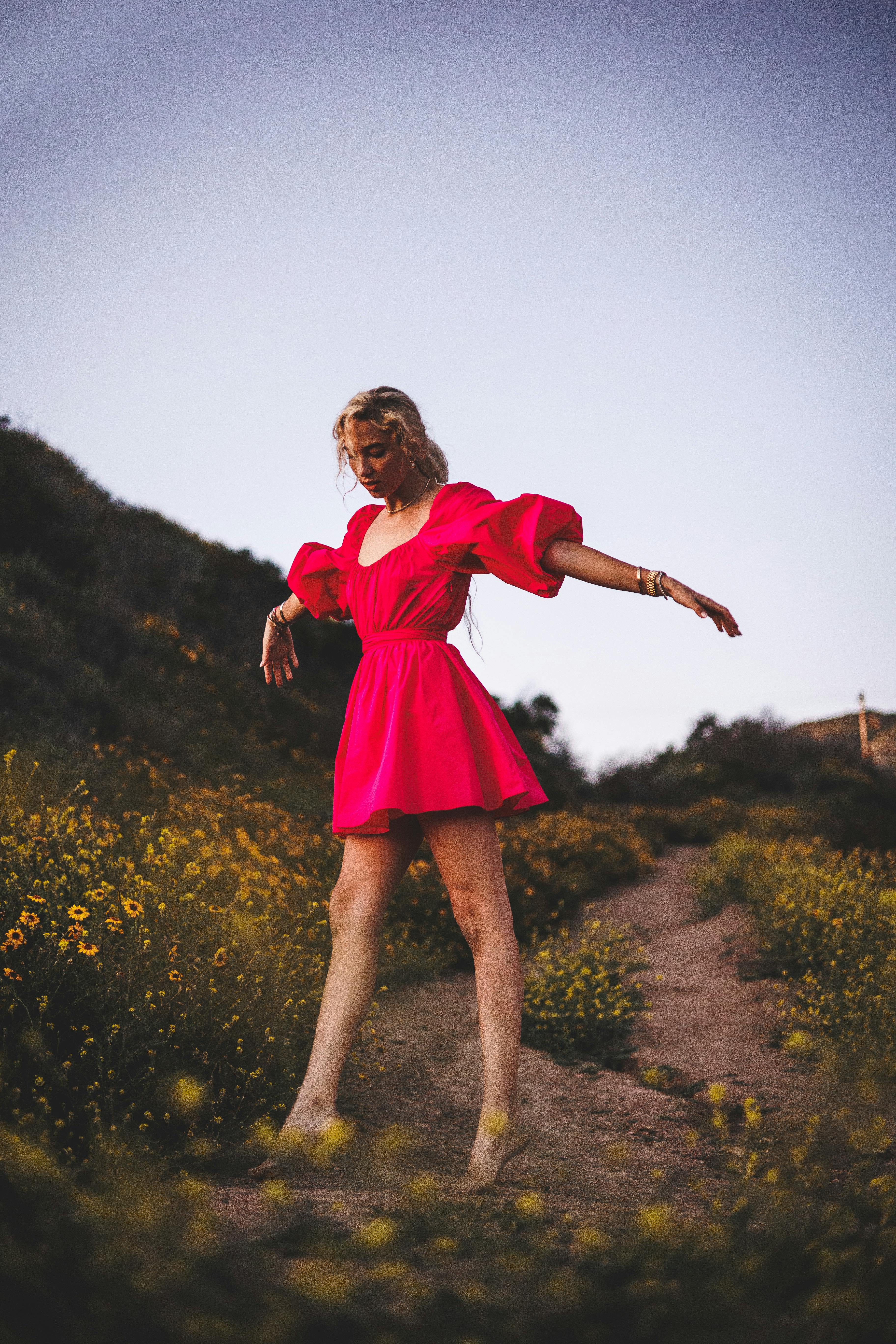 Young woman in a vibrant red dress walking barefoot along a blooming flower path in Malibu.