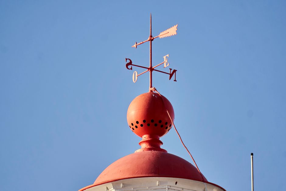 A weather vane atop a red dome under a clear blue sky, symbolizing direction and weather changes.