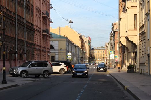 An urban street scene with classic architecture, vehicles, and pedestrians on a sunny day.