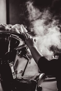 Monochrome close-up of a barista's hand using an espresso machine with visible steam.