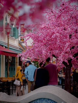 Vibrant cherry blossoms in full bloom enhance a lively urban street scene with pedestrians.