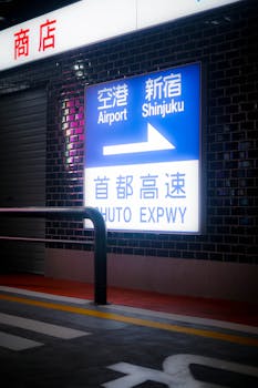 A night view of a Shinjuku highway sign pointing to the airport, taken indoors with subdued lighting.