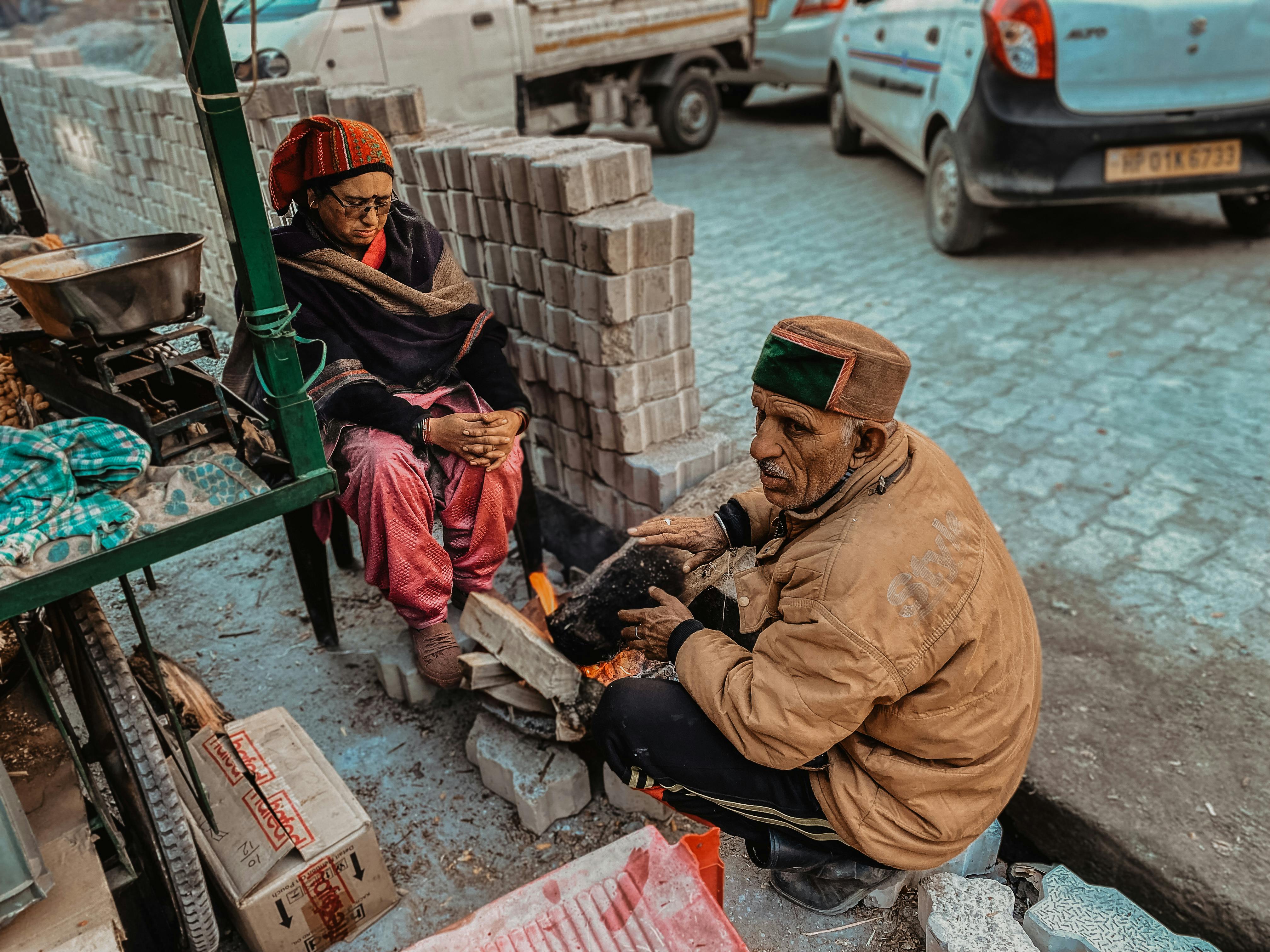Elderly couple warming by a street fire in an urban setting on a cold day.