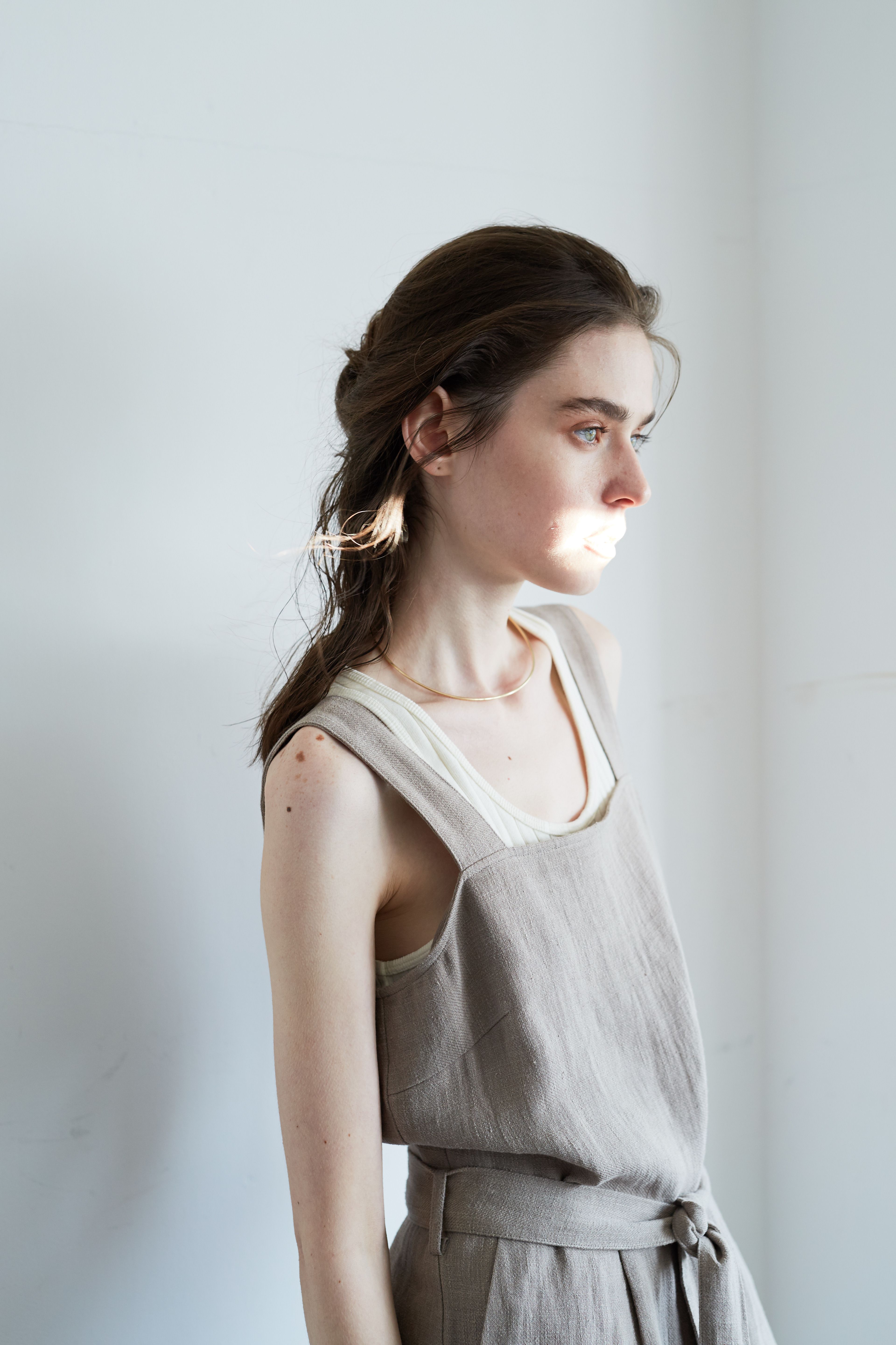 Elegant woman in linen dress standing in sunlit room with soft natural lighting.