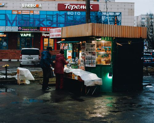 Free Street kiosk in a rainy city evening selling newspapers and magazines with two people interacting. Stock Photo