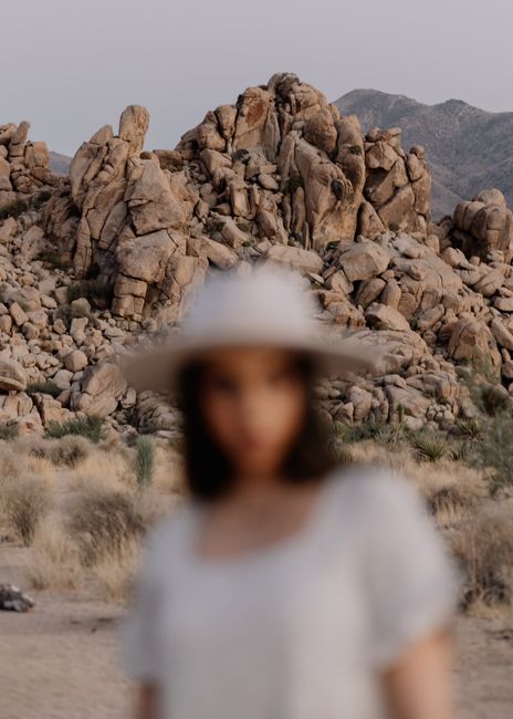 Blurred portrait of a woman wearing a hat against rocky desert backdrop in California.