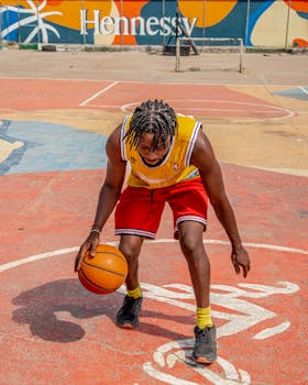 A young man dribbles a basketball on a vibrant outdoor court with colorful mural backdrop.