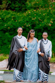 Three people in traditional African attire posing outdoors for wedding photography.