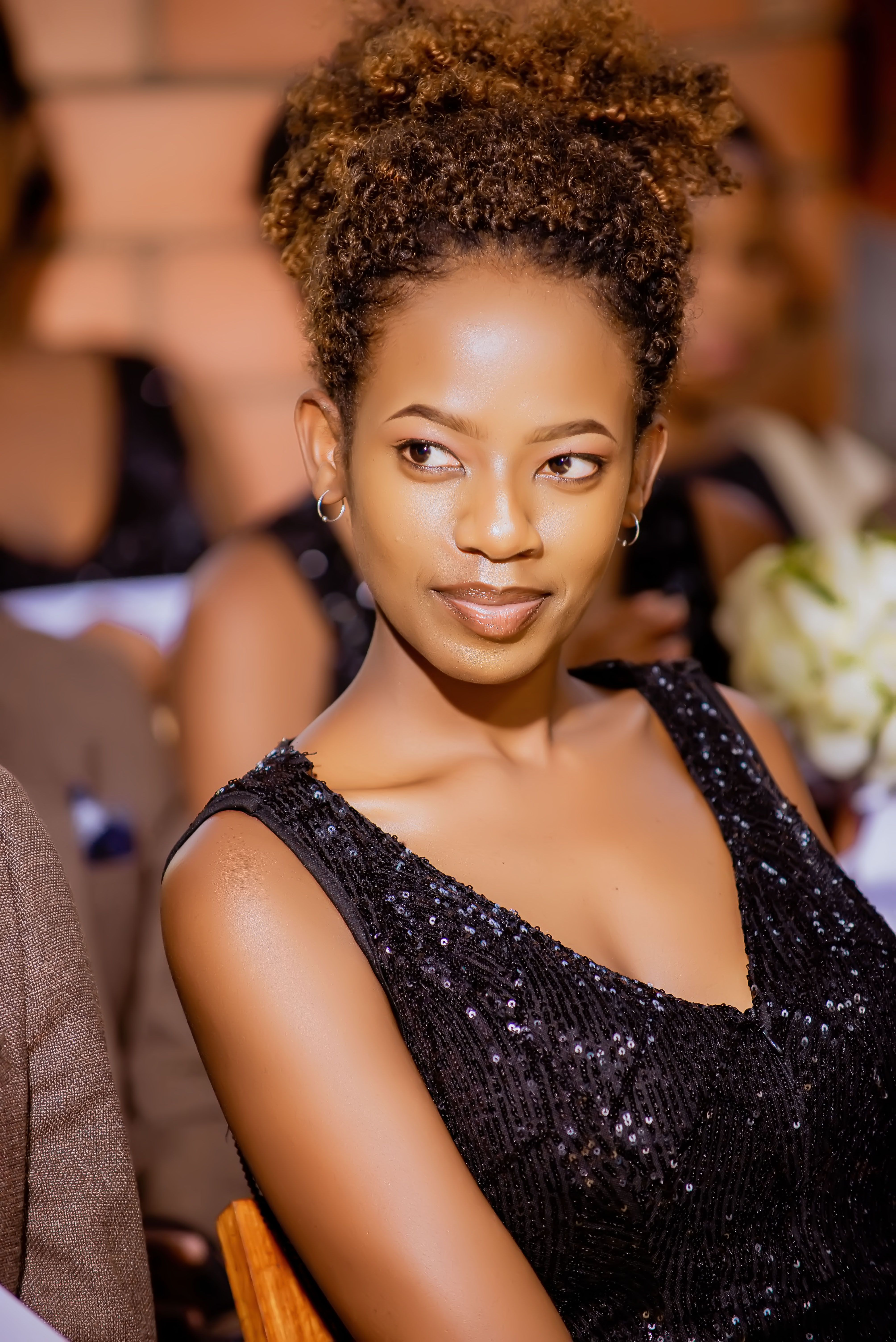 A stylish woman in a black dress with afro hair attending a formal event indoors.
