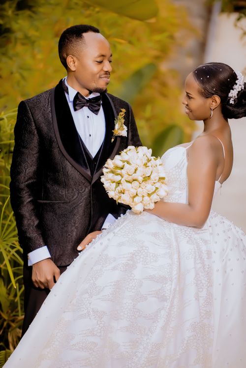 Free Couple in elegant wedding attire, sharing a tender moment outdoors with a white flower bouquet. Stock Photo