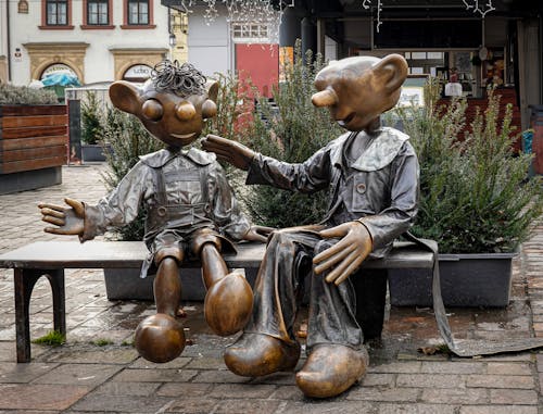 Brass Statues of Cartoon Characters Sitting on Bench