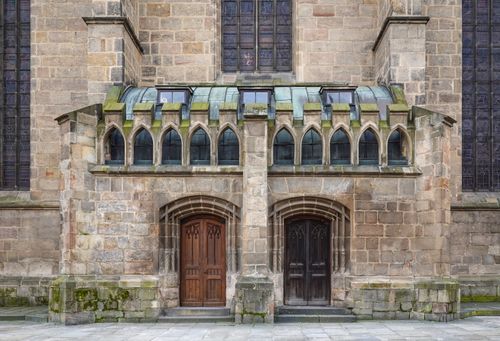 Free Historic church facade with Gothic architectural elements featuring arched windows and two wooden doors. Stock Photo