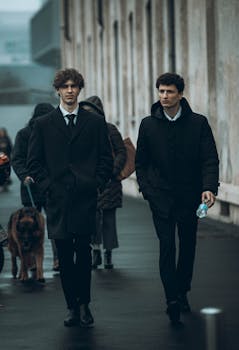 Two young men in business attire walking on an urban street with historic architecture.