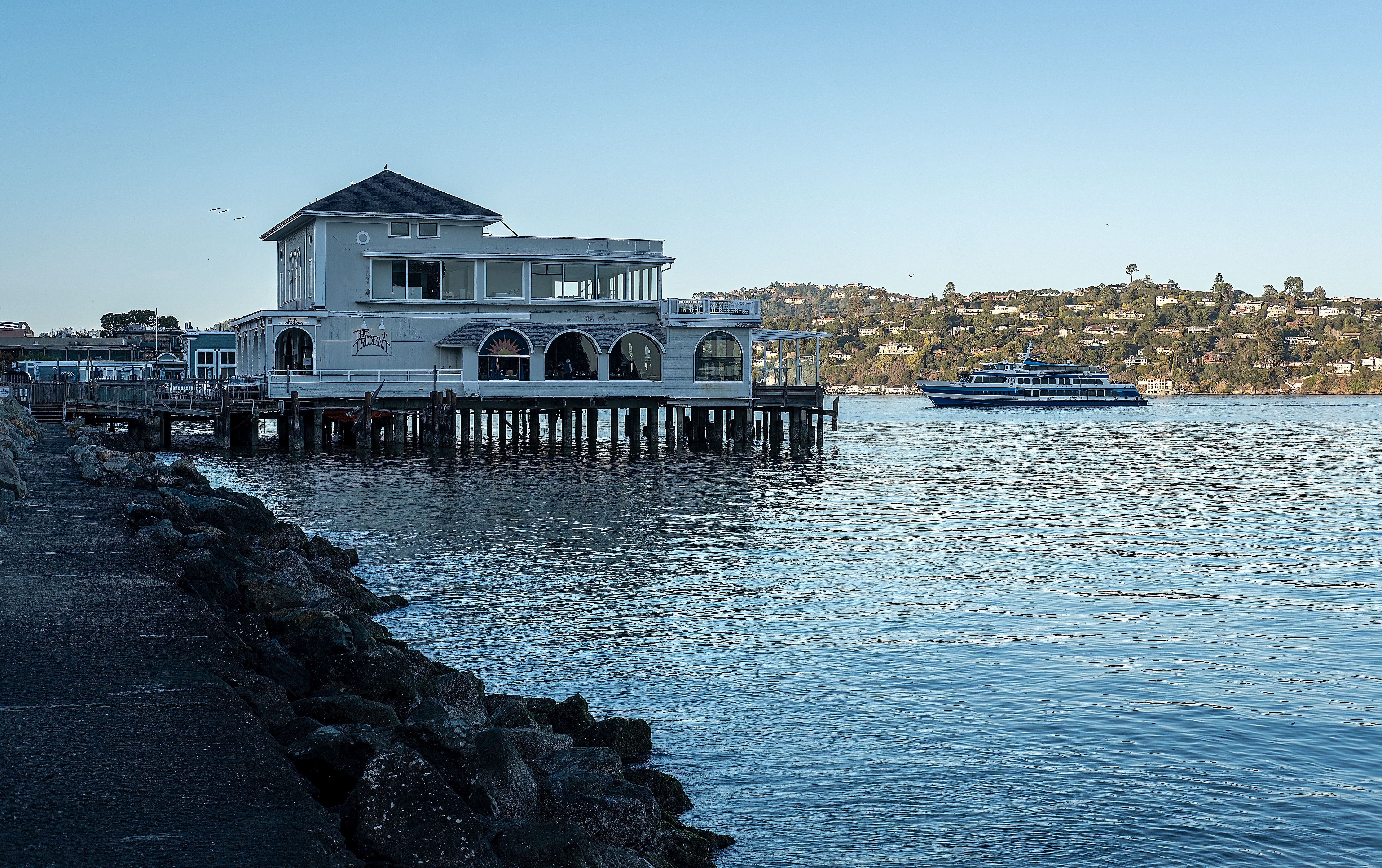 Elegant waterfront restaurant by the sea with a ferry in the background, creating a tranquil scene.