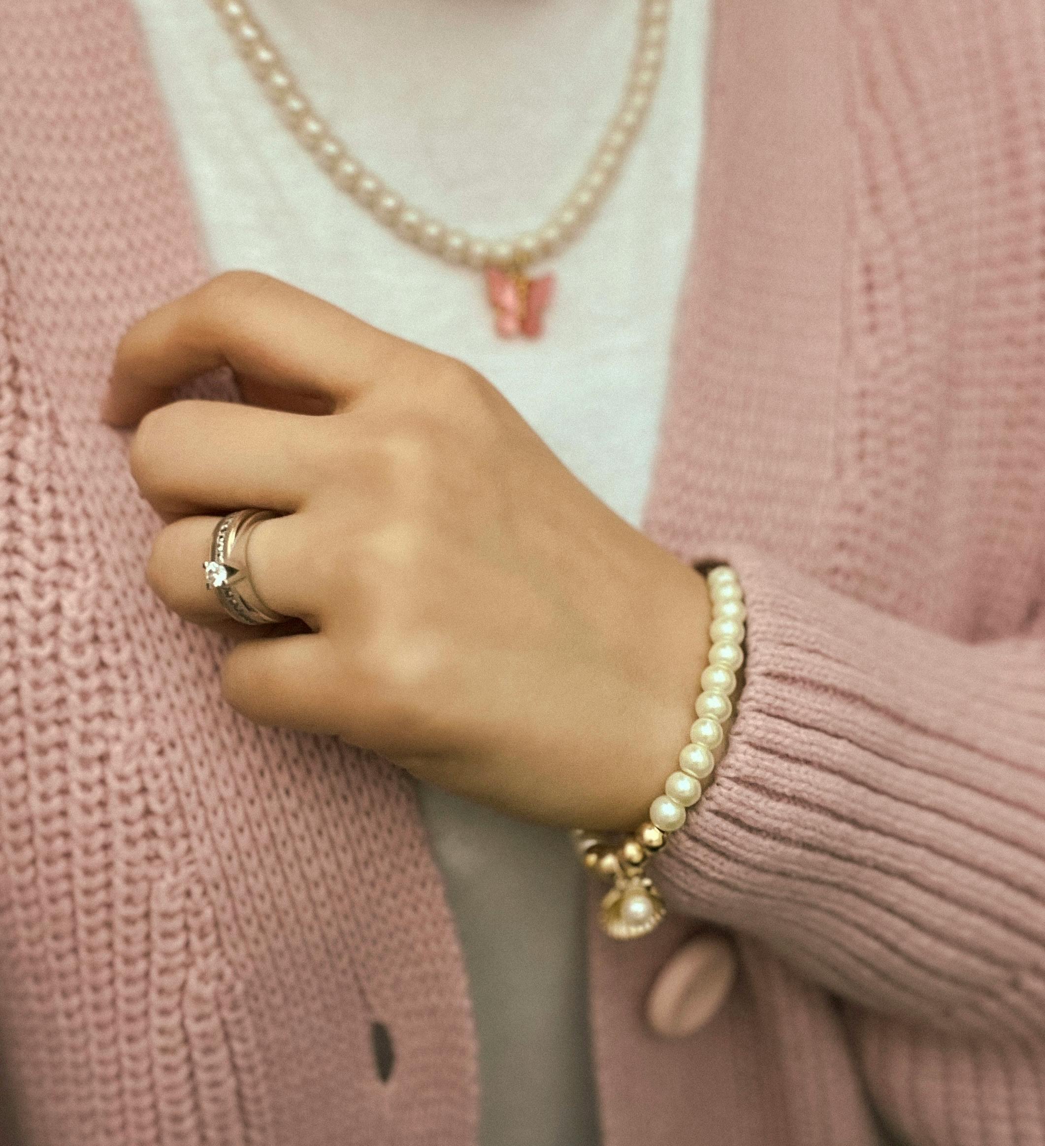 Close-up of a woman's hand showcasing elegant jewelry and a pink cardigan.