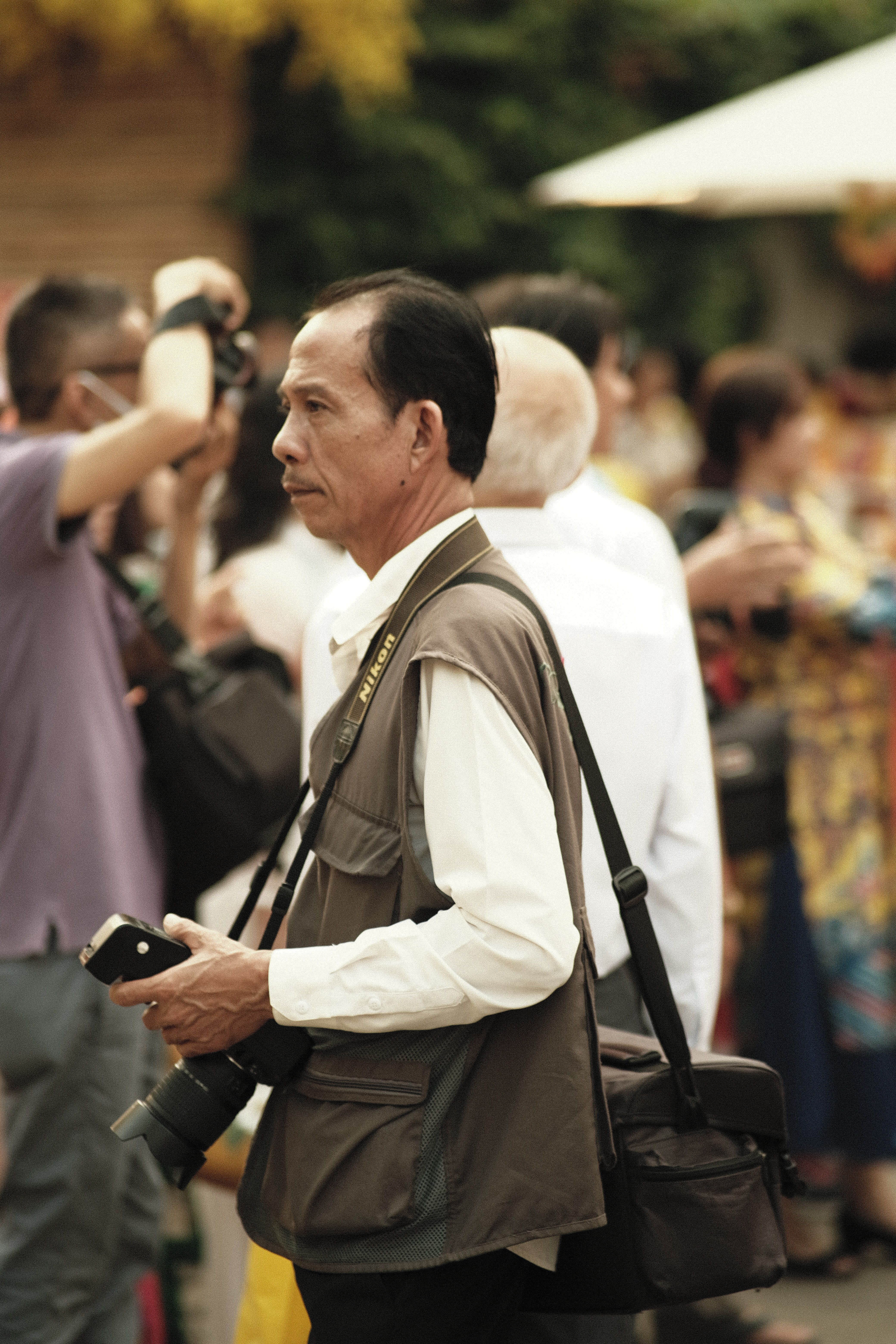A photographer stands amidst a bustling street scene in Hồ Chí Minh City, capturing urban life.