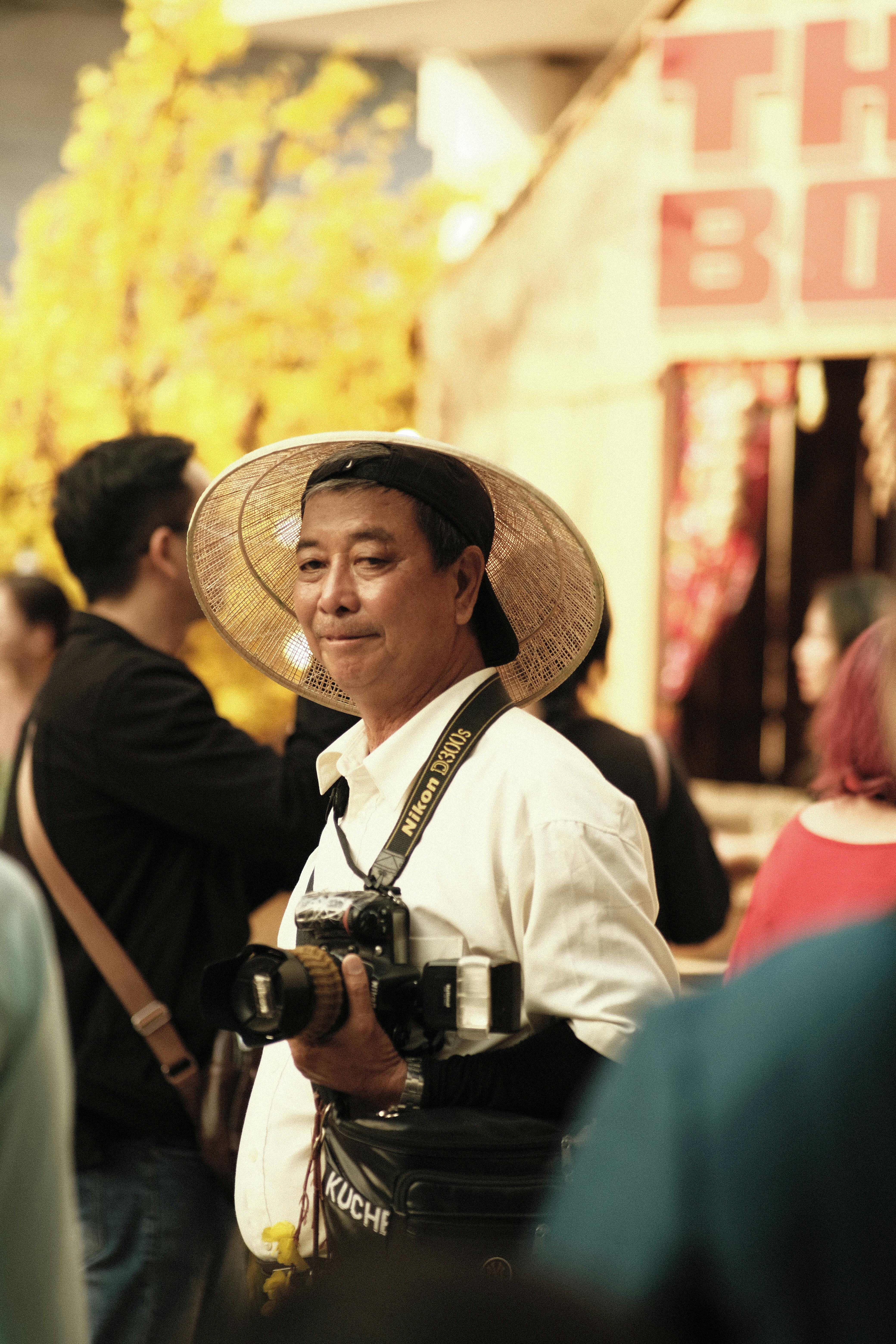 Capture of a man in a conical hat with a camera at a vibrant cultural festival in Ho Chi Minh City, Vietnam.