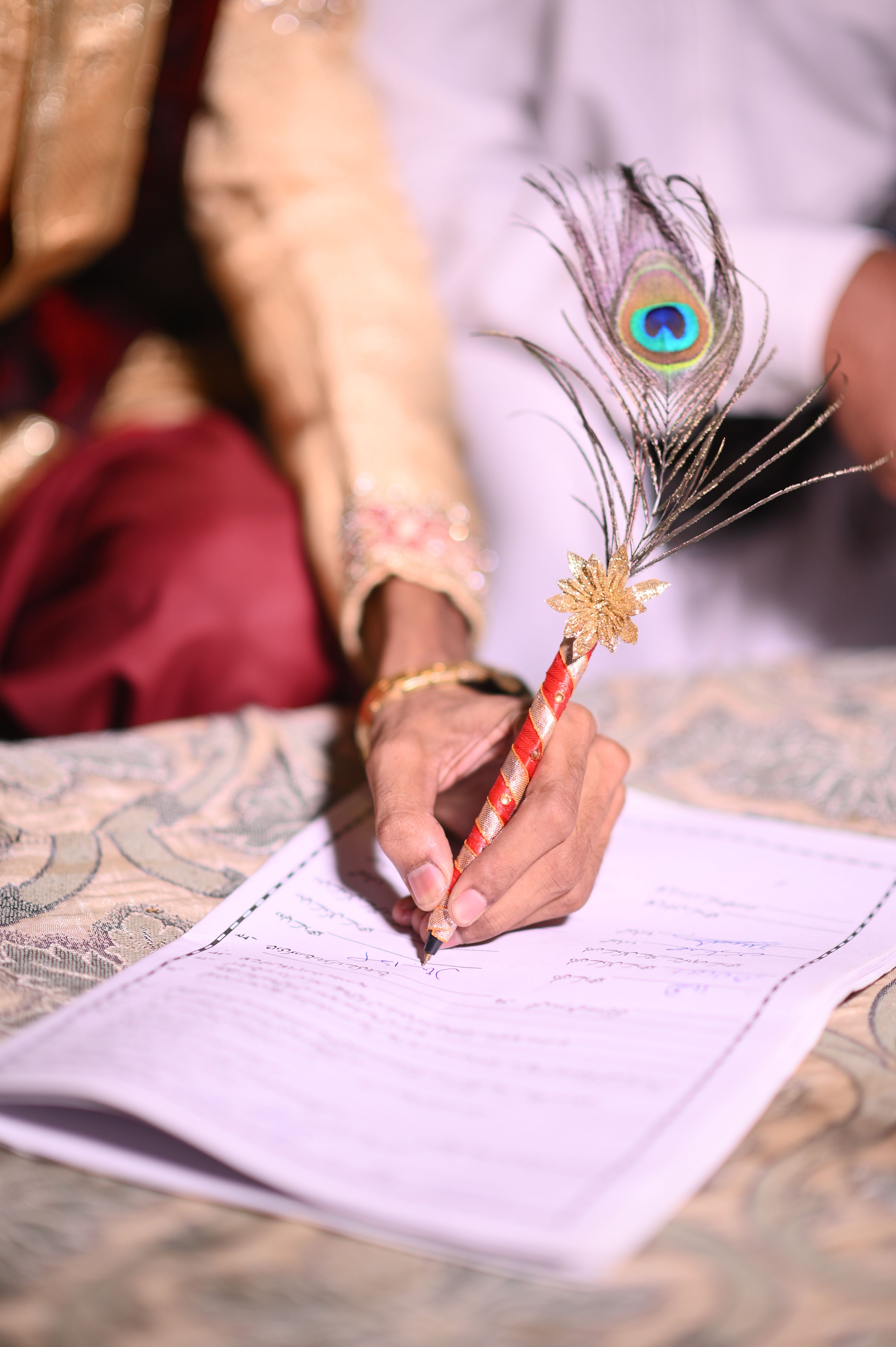 Close-up of a South Asian wedding ceremony signing with a peacock feather pen.