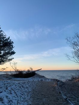 A tranquil winter beach scene with snow-covered dunes and a beautiful sunrise over the calm ocean.