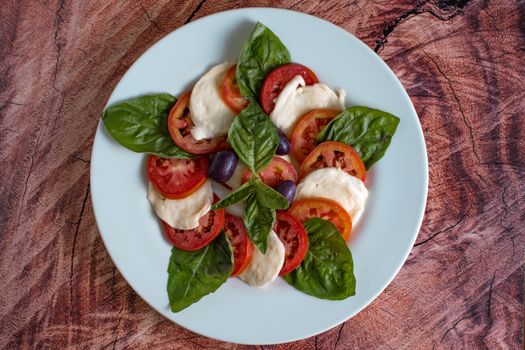 Top view of a fresh Caprese salad featuring tomatoes, mozzarella, basil, and olives.