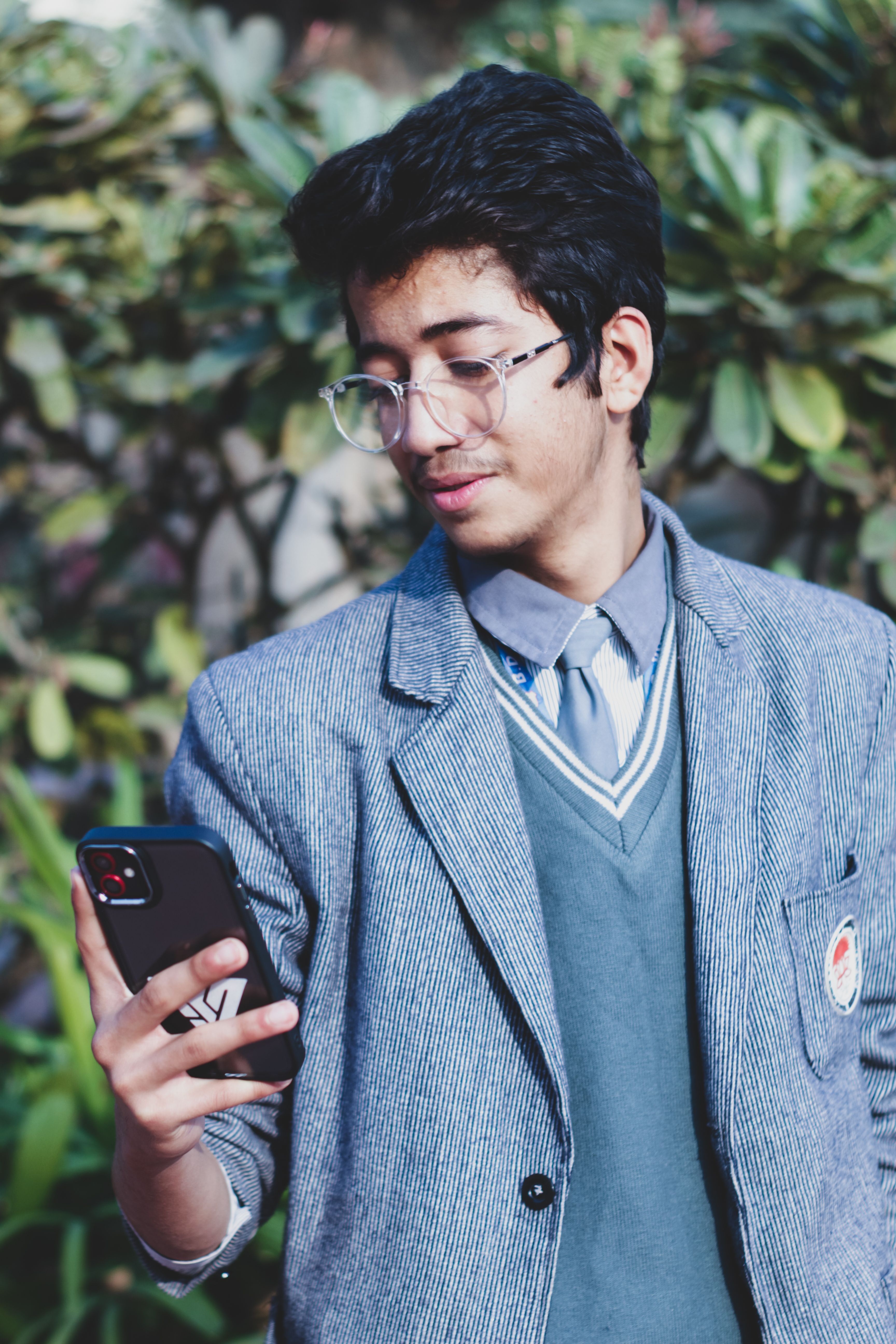 Young South Asian man in uniform standing outdoors, using smartphone and smiling.