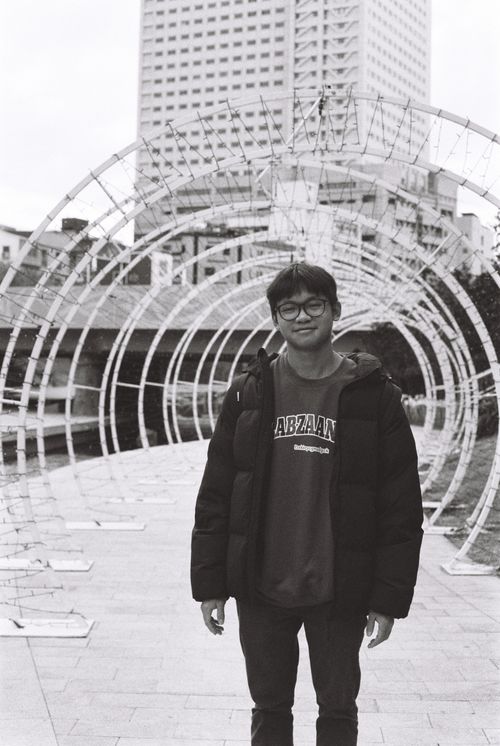 Free A young man smiles confidently standing outdoors in a black and white urban scene. Stock Photo