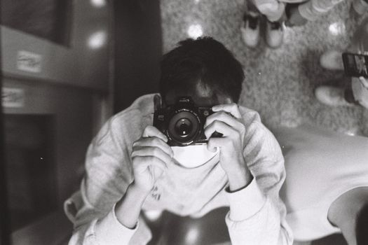 Artistic black and white mirror selfie featuring a person holding a camera indoors.