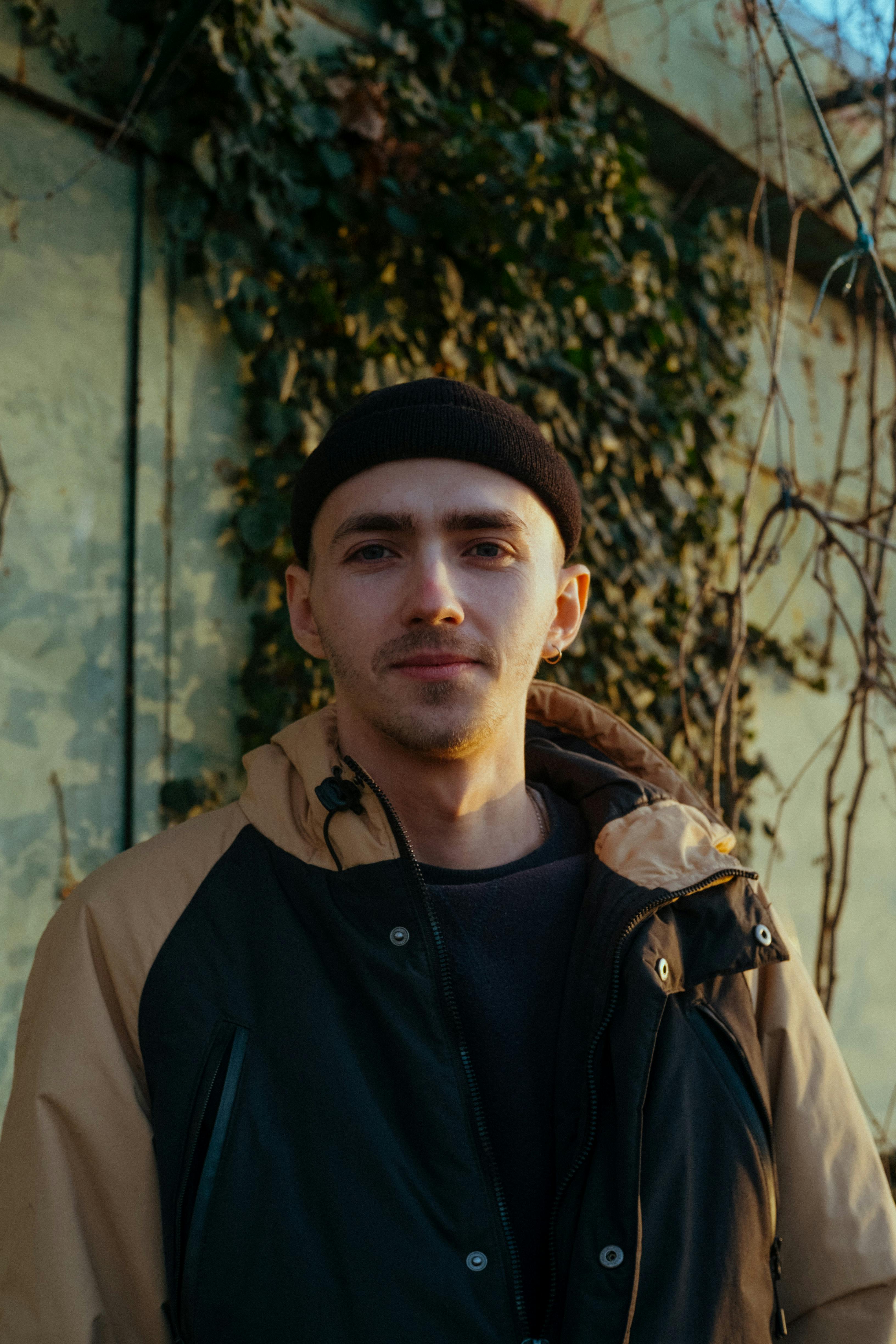 Portrait of a young man smiling in winter attire against an outdoor ivy background.