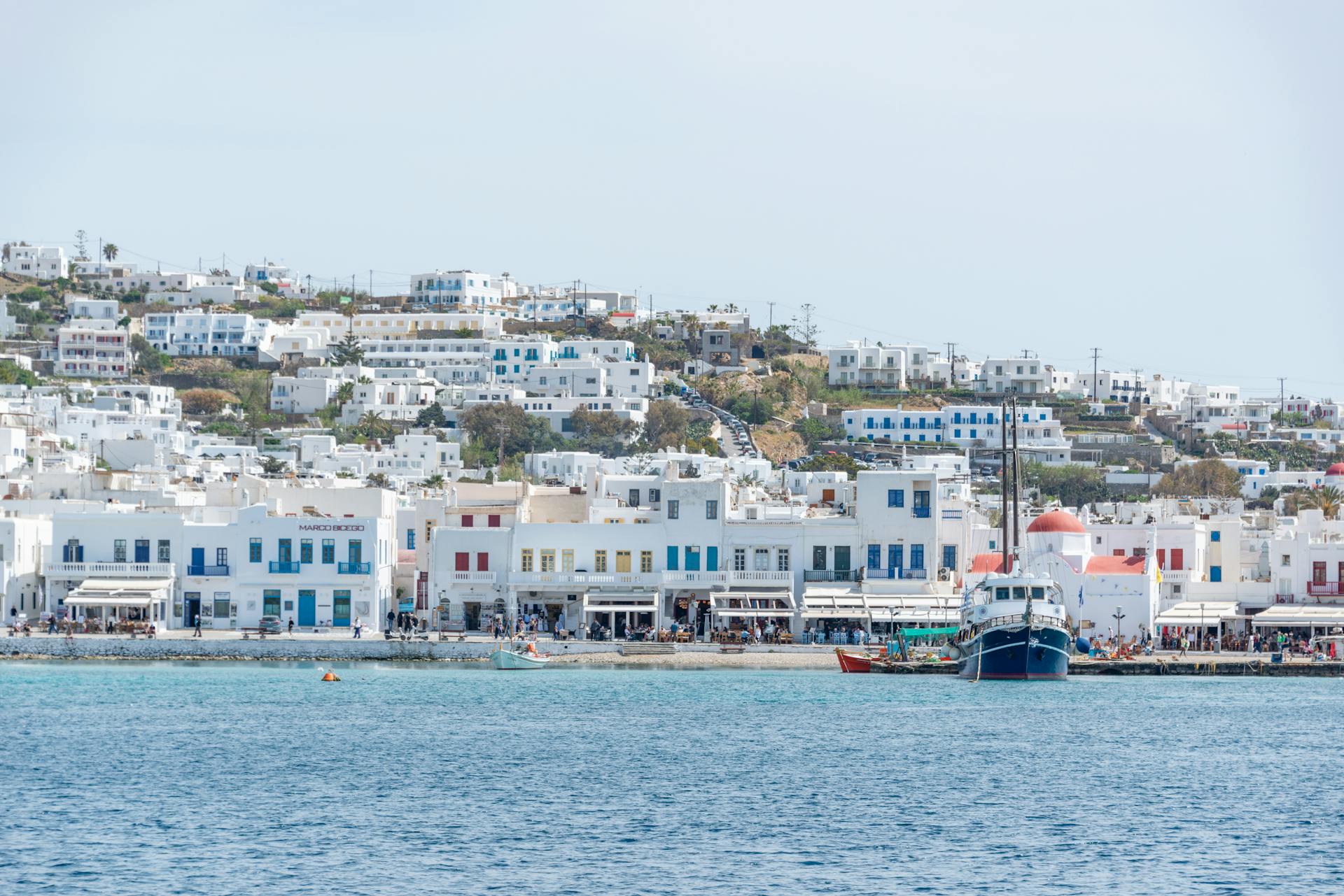 Charming Mykonos harbor with white Cycladic buildings and a colorful ship.